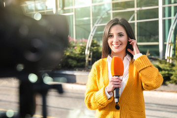 Wall Mural - Young female journalist with microphone working on city street