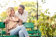 © Kawee - Caucasian senior elder couple sit on bench in park. Mature are happy and enjoy with slow life. Old man love, hug woman from behind. They look and smile together. Retirement family lifestyle concept.