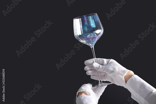 Person in white gloves checking cleanliness of glass on dark background, closeup. Space for text