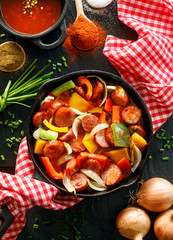 Wall Mural - Stew with peppers and sausage in a cast iron skillet on a black background, top view. Traditional Hungarian dish called lecho