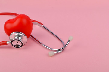 Red heart with stethoscope on pink background. Heart health care concept. Selective focus.