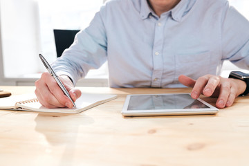 Aufkleber - Close-up of unrecognizable businessman sitting at desk and using tablet while making notes about promotion statistics