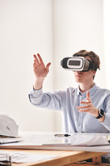 Aufkleber - Male engineer sitting at desk and gesturing hands while designing 3D model of building with VR device