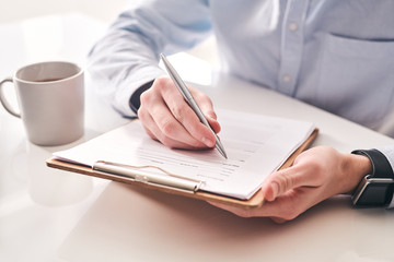 Poster - Close-up of unrecognizable businessman sitting at table with tea mug and making notes in application form
