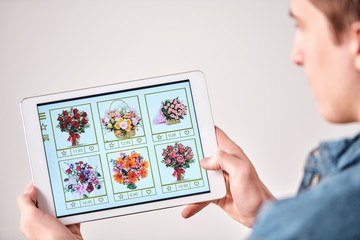 Poster - Over shoulder view of young man choosing flower bouquet for girlfriend using catalogue in online store