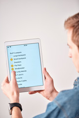 Aufkleber - Over shoulder view of young man using packing list in tablet note while putting checkmark in packed stuff