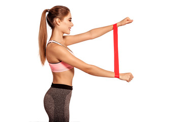 Beautiful, woman stands in sportswear. Strong, athletic body, thin, flat stomach. Sport woman doing arm exercises with fitness gum, use elastic band for sport. White background, isolate.