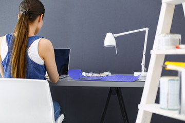 Young woman sitting at the desk with instruments, plan and laptop.