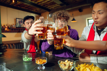 Wall Mural - Sport fans cheering at bar, pub and drinking beer while championship, competition is going. Multiethnic group of friends excited watching translation. Human emotions, expression, supporting concept.