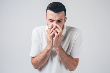 Young man isolated over background. Sick person with nose running. Using white napkin. Coronavirus danger. Ill male person inside studio room.