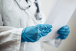 © Konstantin Zibert - Closeup of a woman doctor wearing white medical gown and blue gloves, stethoscope. Female nurse holding papers with diagnosis for a patient. Coronavirus, covid-19 and sickness prevention concept.