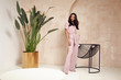 © indiraswork - Beautiful sexy brunette woman tanned skin face cosmetic makeup wear pink suit pants for date walk office fashion clothes style collection interior room  sand color safari summer armchair palm boho.