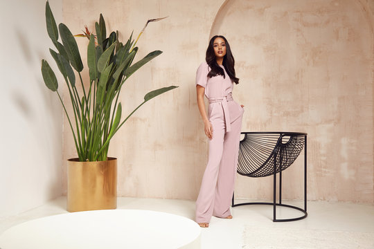 Wall Mural -  - Beautiful sexy brunette woman tanned skin face cosmetic makeup wear pink suit pants for date walk office fashion clothes style collection interior room  sand color safari summer armchair palm boho.