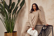© indiraswork - Beautiful sexy brunette woman face  tanned skin wear fashion clothes style collection beige knitted suit sandals accessory bag interiorfurniture armchair journey summer wall flowerpot palm boho.