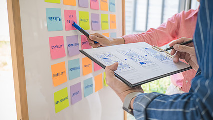 Web designer brainstorming for a strategy plan. Colorful sticky notes with things to do on office board. User experience (UX) concept.