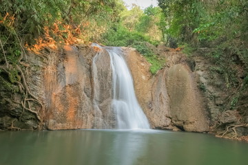 view of silky waterfall flowing from rock cliff around with green forest background, Nang Kruan Waterfall, Lam Klong Ngu National Park, Kanchanaburi, west of Thailand.
