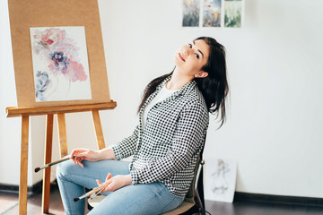 Artwork, creativity and inspiration. Young woman sitting at easel painting with watercolors. Drawing studio