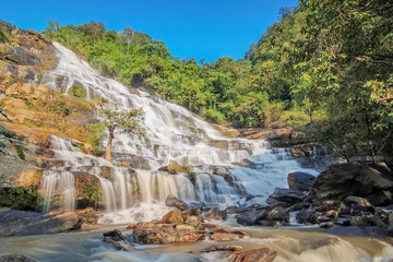 view morning of silky waterfall flowing on cliff rocks around with green forest and blue sky background, Mae Ya Waterfall, Doi Inthanon National Park, Chiang Mai, northern of Thailand.