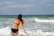 Back view of young woman in black bikini enjoying the wavy sea during her vacation. Beautiful fit woman entering the sea.