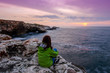 Young woman tourist watching sunset on the edge of the cliff.Hiking woman sit on mountain rock watching the sunrise at the sea