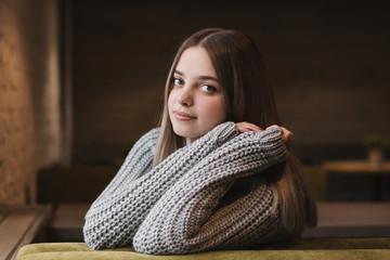 Horizontal portrait of young female with long hair and in knitted sweater sitting alone indoors. Teenage girl