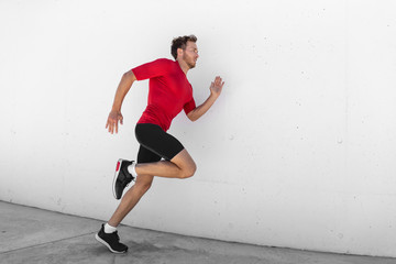 Wall Mural - Running man jogging fast profile sideways against white wall outdoor background. Male athlete training healthy active lifestyle.