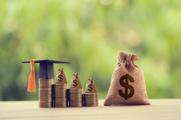 Black graduation cap, Hat and US dollar bag on rows of rising coins,  on a table. Education funding, financial concept. Depicts savings for child knowledge for future studies