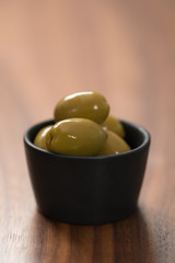 giant green olives in black bowl on walnut table