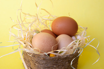 Wicker basket with Easter eggs and candy on yellow background