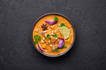 A Chicken Massaman Curry in black bowl at dark slate background. Massaman Curry is Thai Cuisine dish with chicken meat, potato, onion and many spices. Thai Food. Copy space. Top view