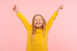 © khosrork - Child sincerely rejoicing success. Cute energetic enthusiastic little girl raising arms in excitement and keeping eyes closed, enjoying victory, winning. indoor studio shot isolated on pink background