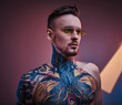 © Fxquadro - Self-assured male model posing in a neon studio with a half-naked body wearing yellow sunglasses and tattooed in a japanese irezumi style, looking cool and relaxed. Close up portrait