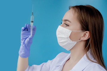 Woman doctor in a white medical coat, mask, hat and gloves holds a syringe with medicine in her hands. Standing on a white background