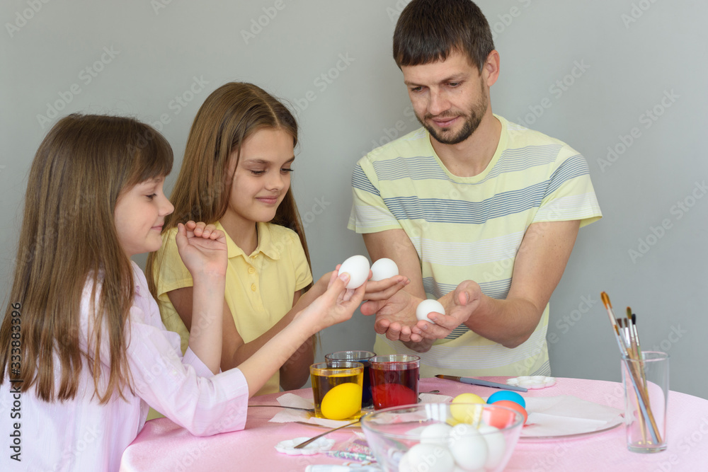 Dad and daughters sit at the table and paint eggs for Easter - obrazy, fototapety, plakaty 