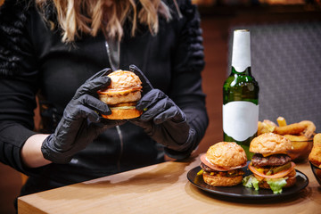 Poster - Female holding small burger, hands in black gloves, beer, fast food