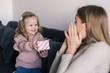 © dianagrytsku - Young mother sitting on the couch at home received a surprise from her daughter looking at the gift in amazement in mother's day.
