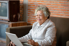 Senior Asian Woman Sit On Sofa Spend Free Time At Home Using Social Networks Having Fun Chatting With Friends Or Children Enjoy New Application,Free Time Advanced Aged User Concept.