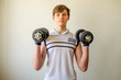 Teenager boy in a white T-shirt is training with two dumbbells.