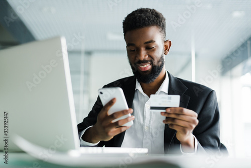 Photographie African American man paying with credit card online while making orders via mobile Internet making transaction using mobile bank application