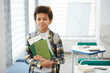 © Seventyfour - Waist up portrait of smiling African-American boy holding books and looking at camera while posing in school classroom, copy space