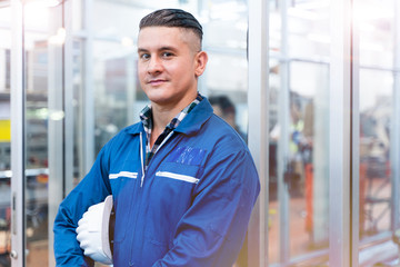 Portrait of manual man worker is standing with confident with blue working suite dress and safety helmet in front the glass wall of high technology clean industry factory.