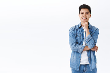 Cheerful, thoughtful and smart asian man in denim jacket, looking satisfied, nod and agree to person suggestion, touch chin smiling pleased, listening to interesting idea, white background