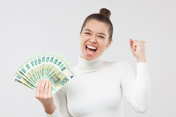 Excited happy young woman holding lots of money, fan of hundred euro banknotes in cash, shouting ot loud. Lottery winner concept.