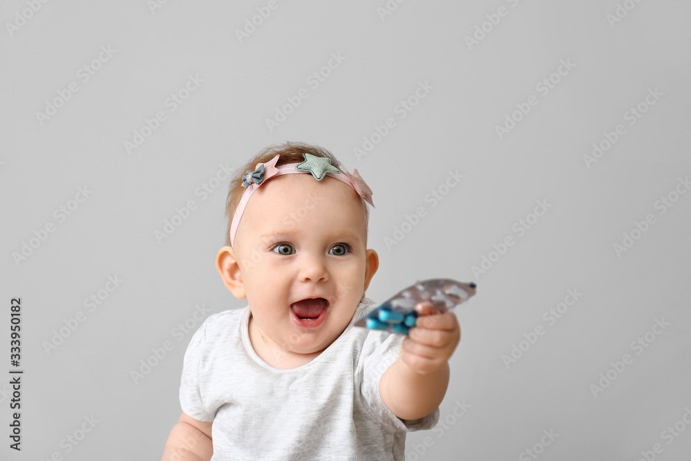 Little baby with medicines on grey background. Child in danger