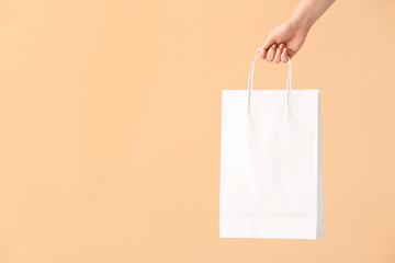 Female hand with paper shopping bag on color background