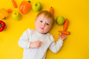 Healthy child nutrition, food background, top view. Smiling baby 8 months old surrounded with different fresh fruits and vegetables on yellow background. Baby first solid feeding.baby with vegetables