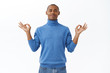 © Cookie Studio - Portrait of calm and patient young african-american man self-isolating at home during pandemia, reaching nirvana during meditating, relaxing with yoga, breathing closed eyes, hands in zen gesture