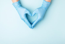 Doctor's Hands In Medical Gloves In Shape Of Heart On Blue Background With Copy Space.
