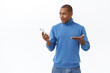 © Cookie Studio - Technology, online lifestyle concept. Portrait of impressed, surprised young african-american man cant believe he won in internet lottery, looking at mobile phone astonished, white background