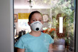 © fivepointsix - Young girl at home in face mask, confined behind window